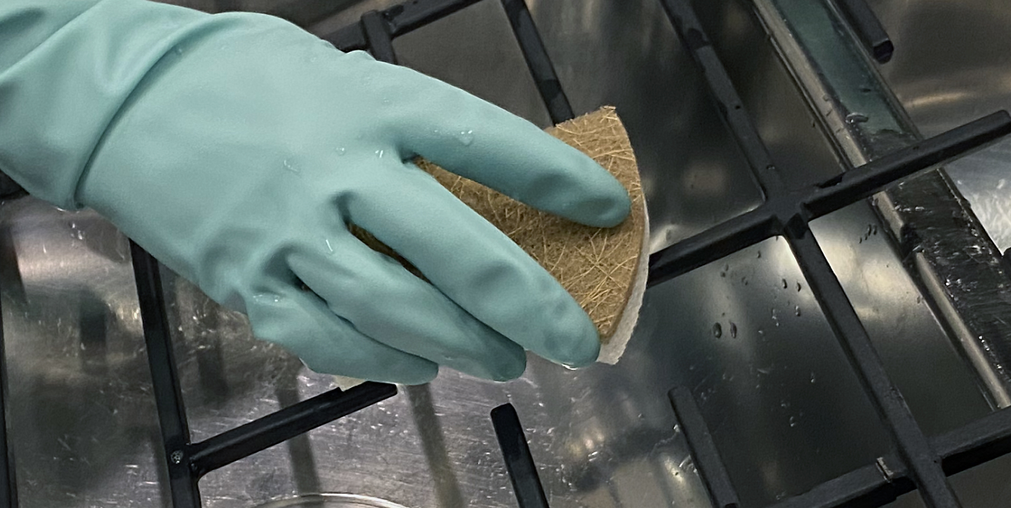 Gloved hand scrubbing range grates with a sponge