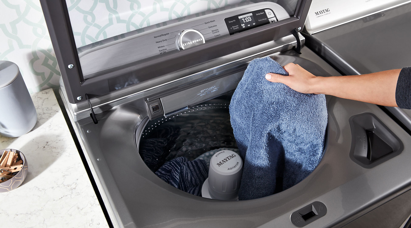Person loading laundry into a top loading Maytag® washer