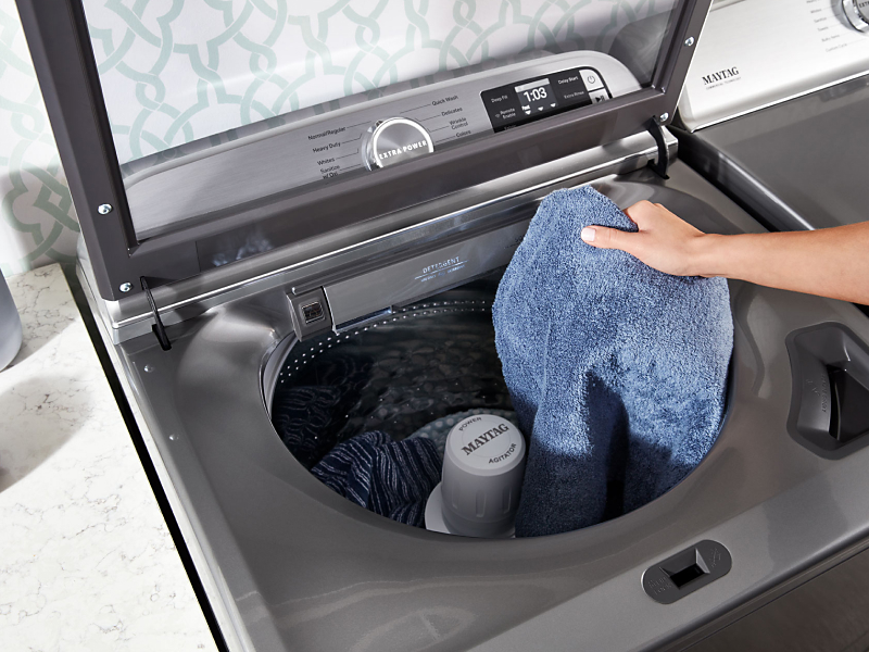 Person loading laundry into a top loading Maytag® washer