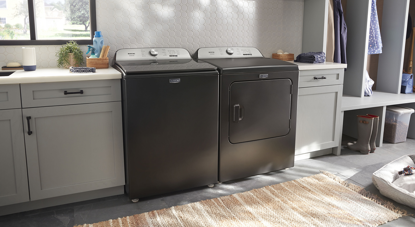 Gray Maytag® top load washer and dryer pair between gray cabinets in laundry room