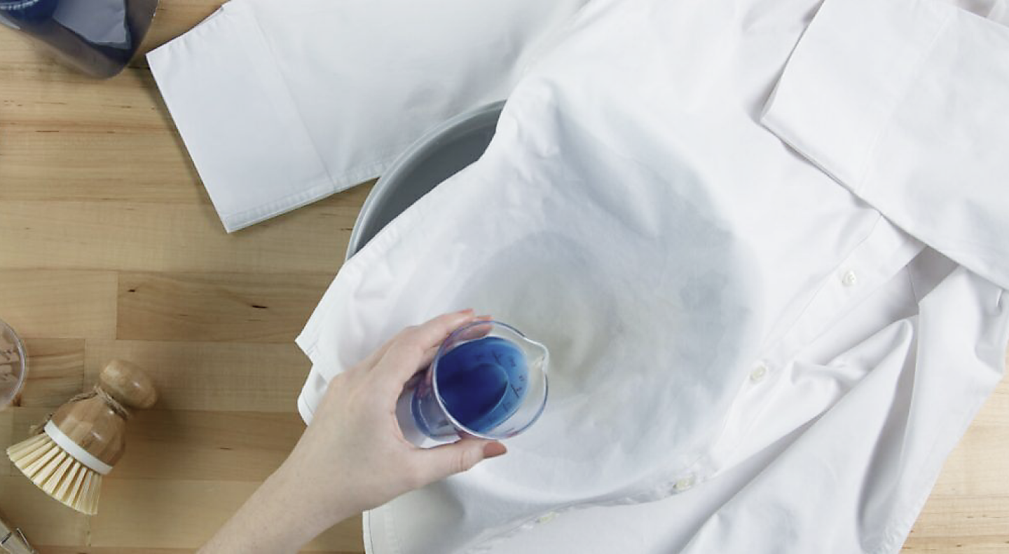 Hand pouring detergent to treat a stain on a button-front shirt
