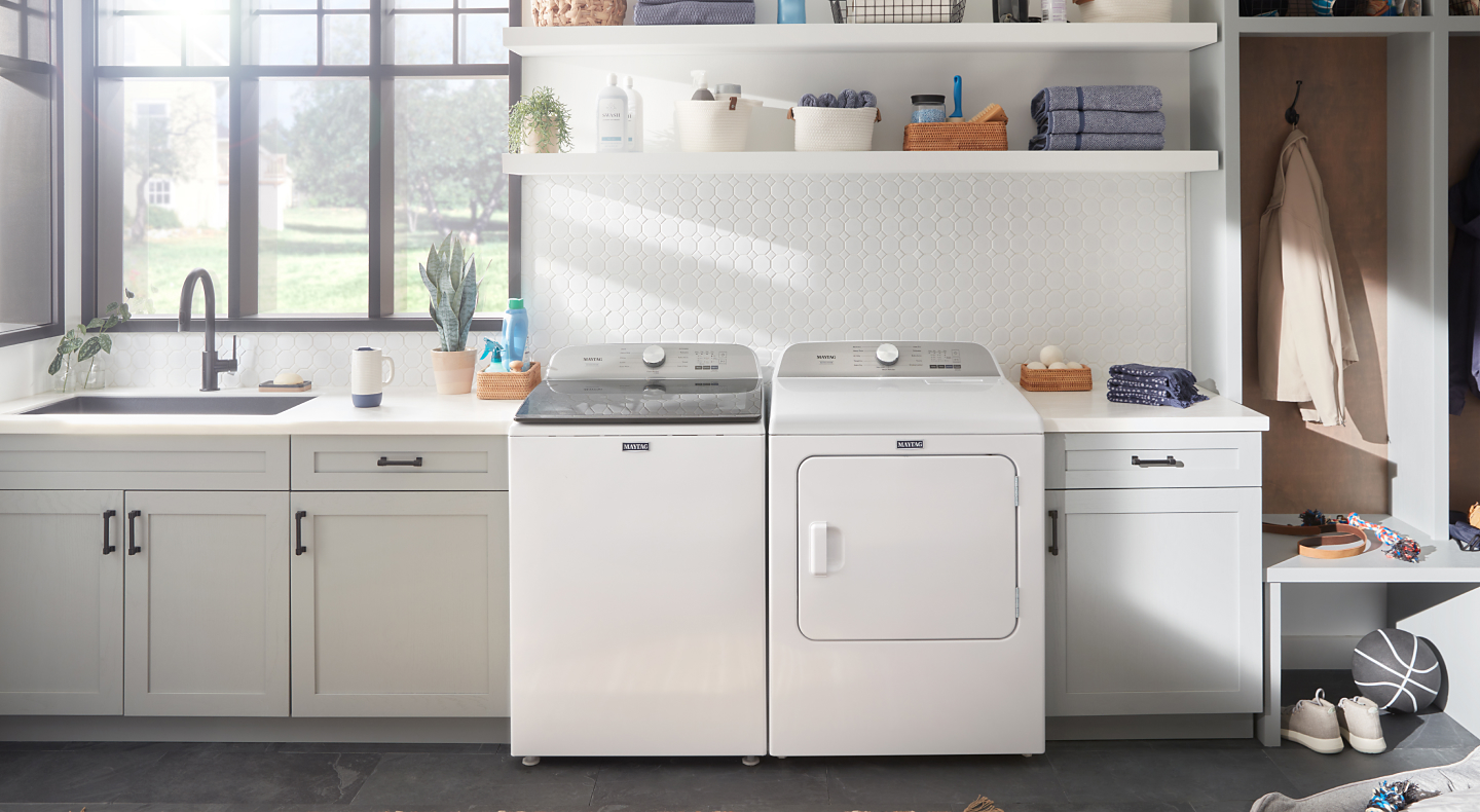 White Maytag® top load washer and dryer pair between cabinets in a laundry room