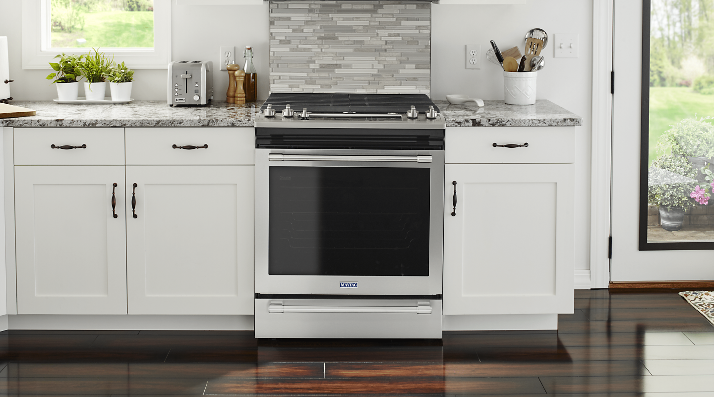 Silver Maytag® gas range surrounded by white cabinetry