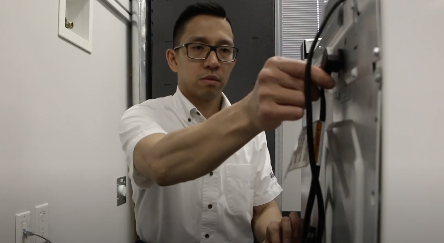 A man freeing the power cord from a Maytag® washing machine. A man freeing the power cord from a Maytag® washing machine.