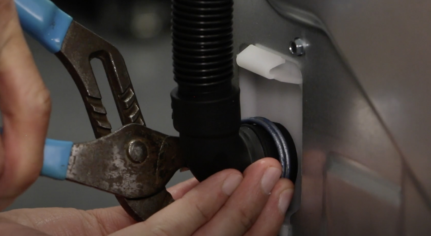 A man securing a drain hose into the drain port of a Maytag® washing machine. A man securing a drain hose into the drain port of a Maytag® washing machine.