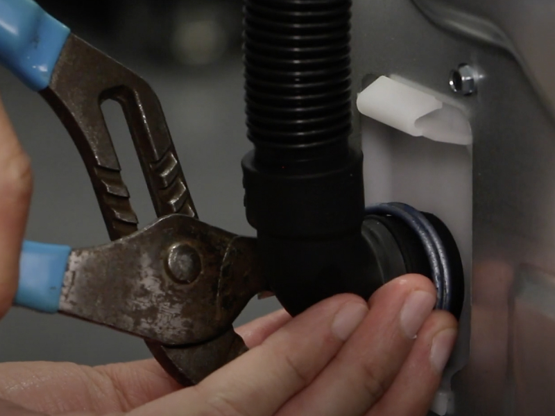 A man securing a drain hose into the drain port of a Maytag® washing machine. A man securing a drain hose into the drain port of a Maytag® washing machine.