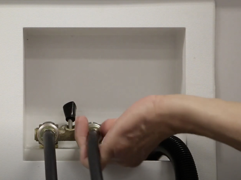 A man connecting the inlet hoses of a Maytag® washing machine to the water faucets.