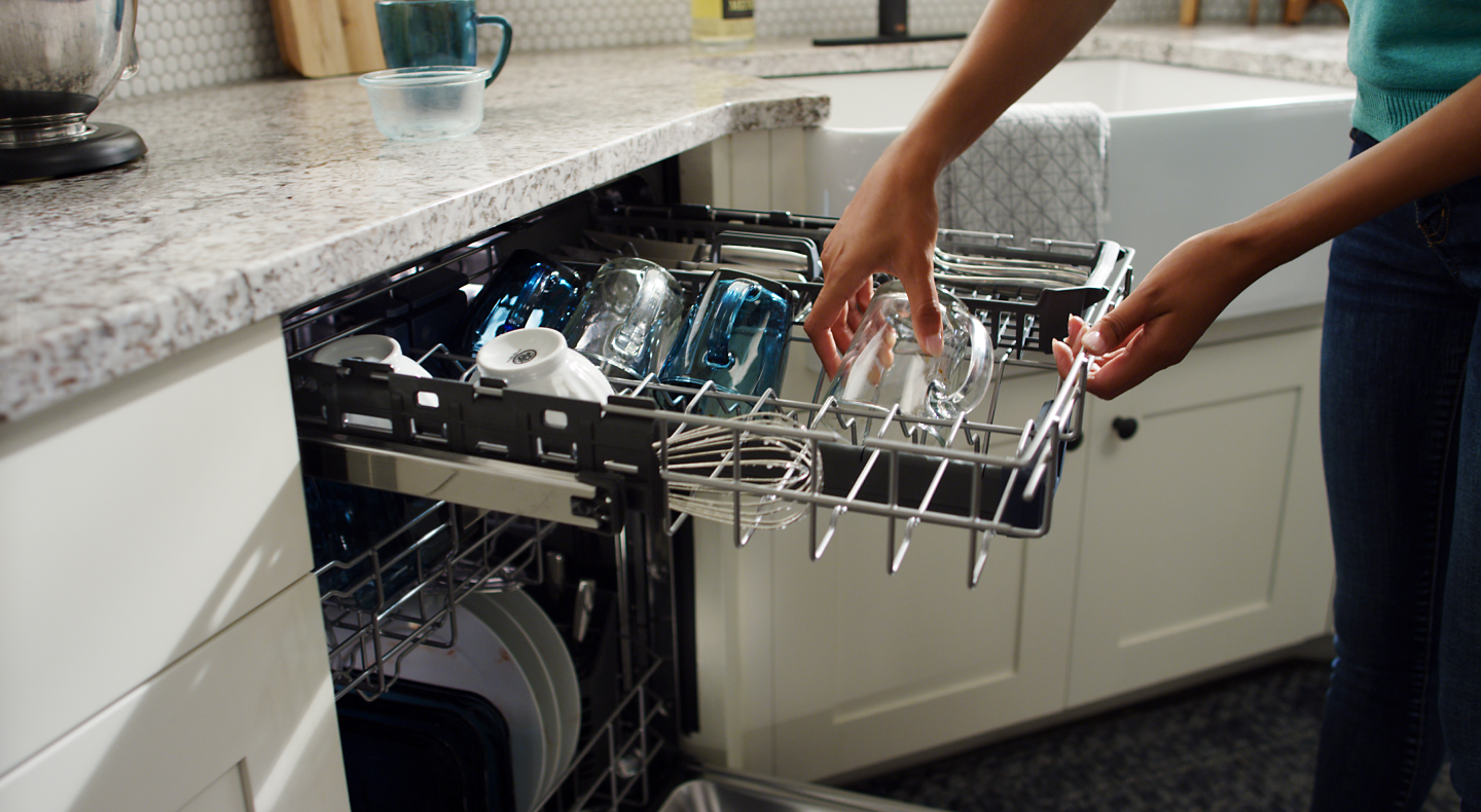 Person loading glasses into a Maytag® third rack dishwasher