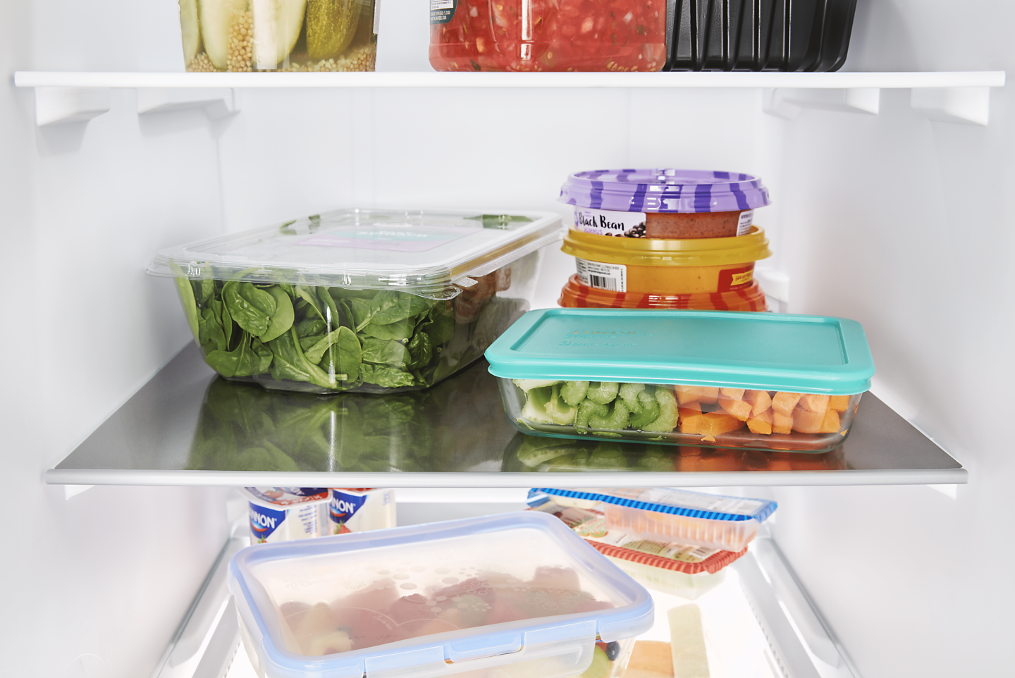 Produce and leftovers in storage containers on the shelf of a fridge