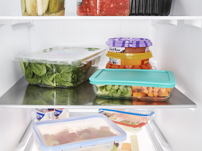 Produce and leftovers in storage containers on the shelf of a fridge