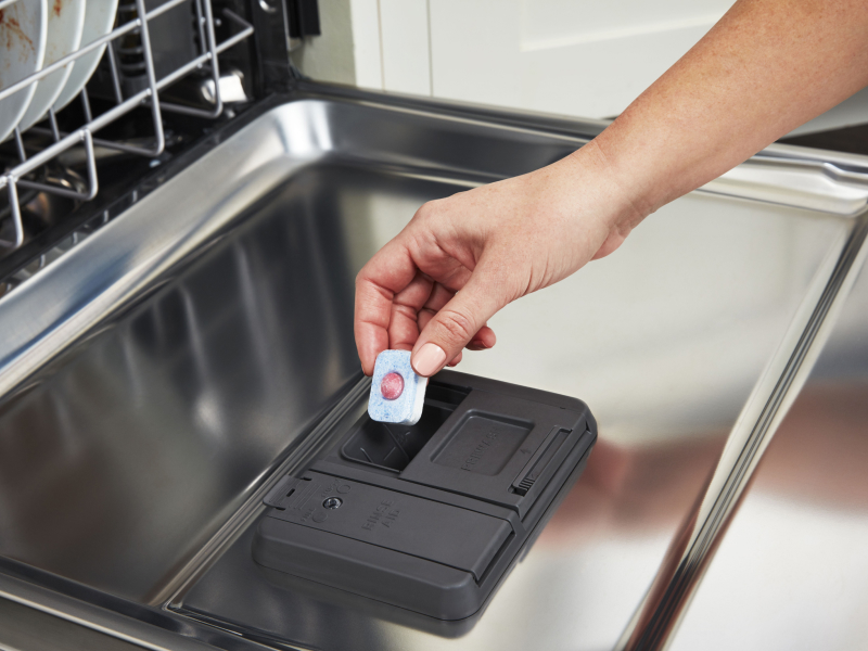 Person loading a detergent pack into a dishwasher.
