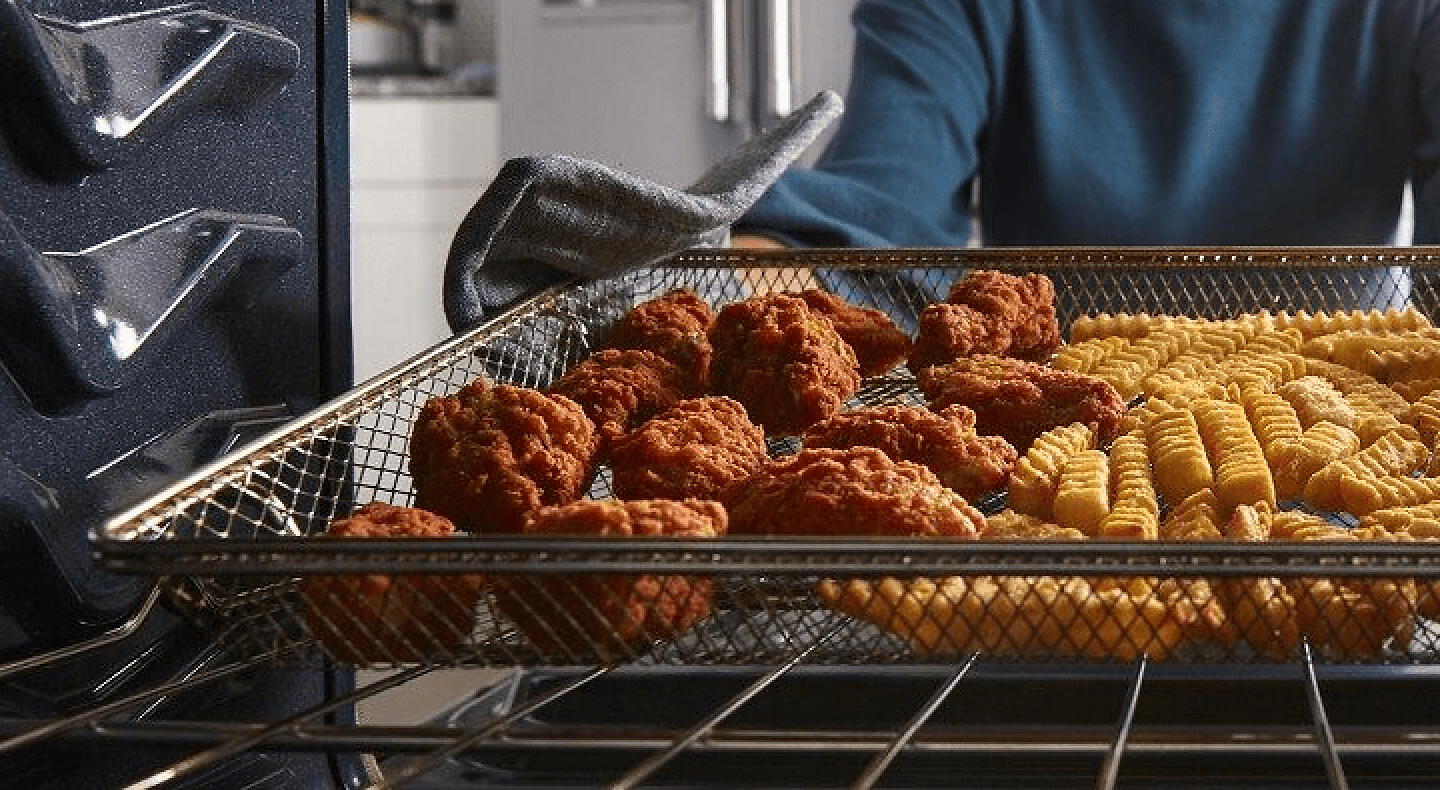 Hand pulling fried chicken and fries out of oven