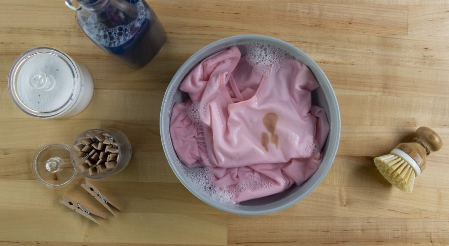 Stained pink blouse soaking in a bowl with cleaning products
