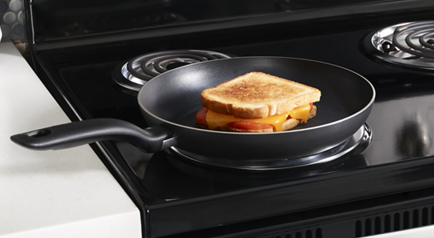 A grilled cheese sandwich in a frying pan on an electric stove with coil burners.