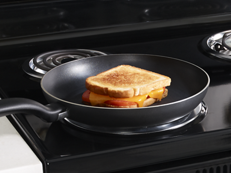 A grilled cheese sandwich in a frying pan on an electric stove with coil burners.