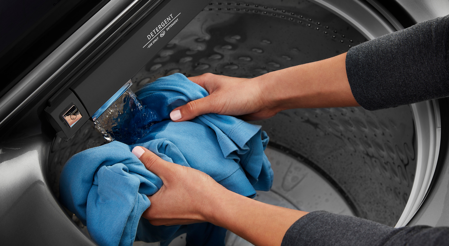 A person rinsing a shirt inside a washing machine.