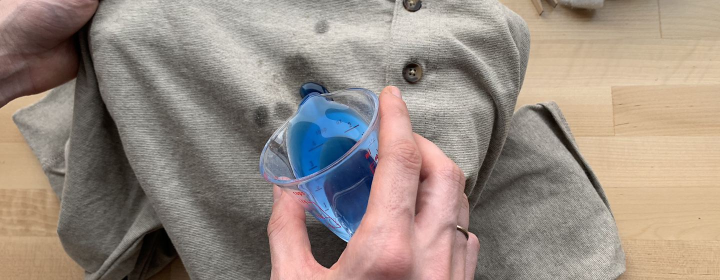 Blue detergent being applied to a gray shirt.
