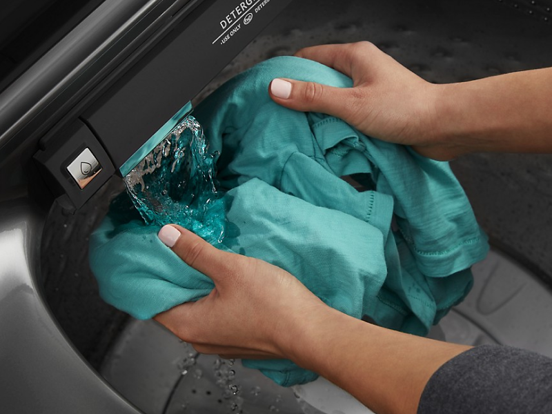 Person using built-in faucet in washing machine to rinse garment