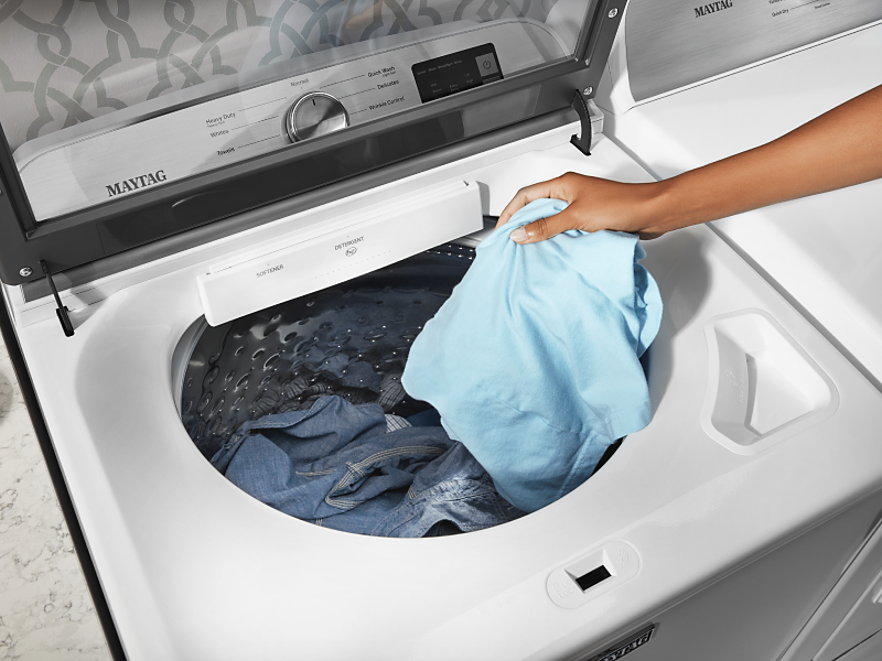 Person putting blue piece of clothing in the washer