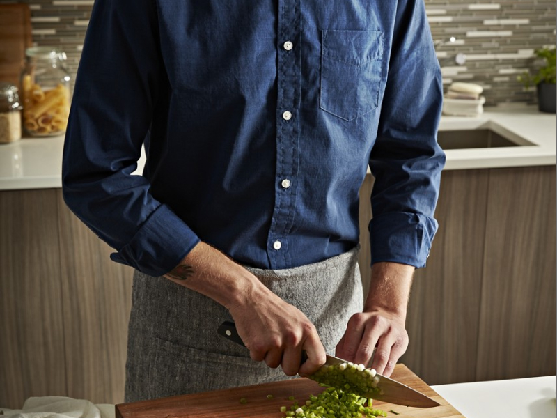 A man chopping broccoli on a cutting board in a modern kitchen with Maytag® appliances