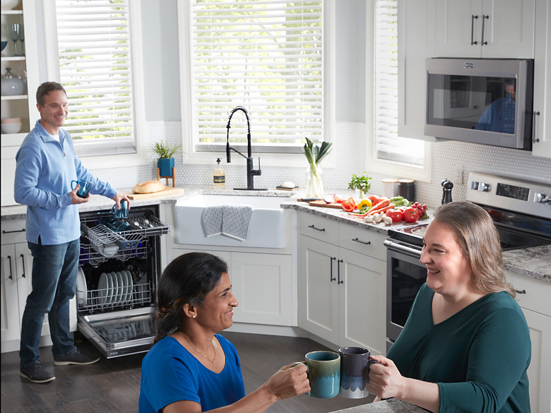 Multiple people in a kitchen with a man emptying a dishwasher