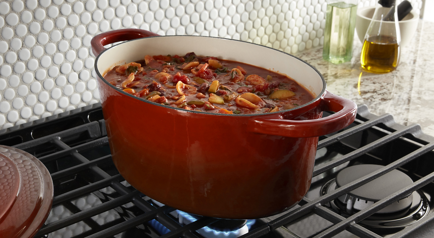 Red dutch oven full of stew simmering above gas burner 