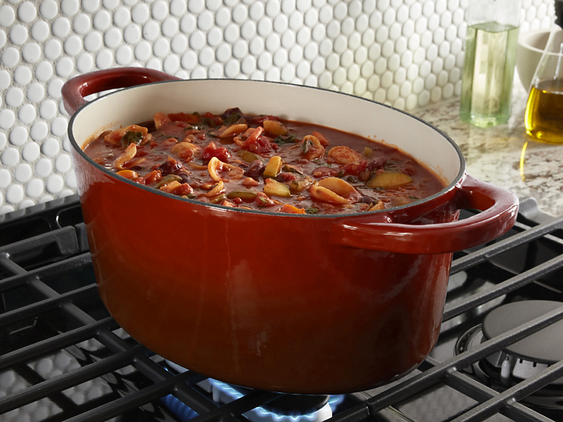 Red dutch oven full of stew simmering above gas burner 