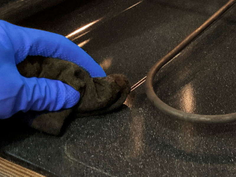 Close-up of hand in blue glove wiping around heat coils in oven cavity