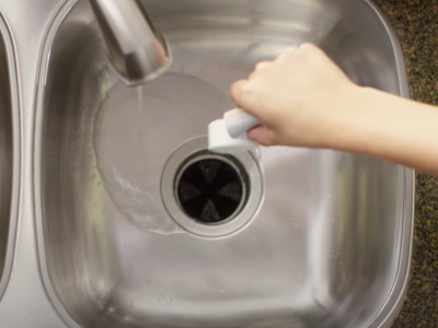 A person dropping an affresh® disposal cleaner tablet down the drain
