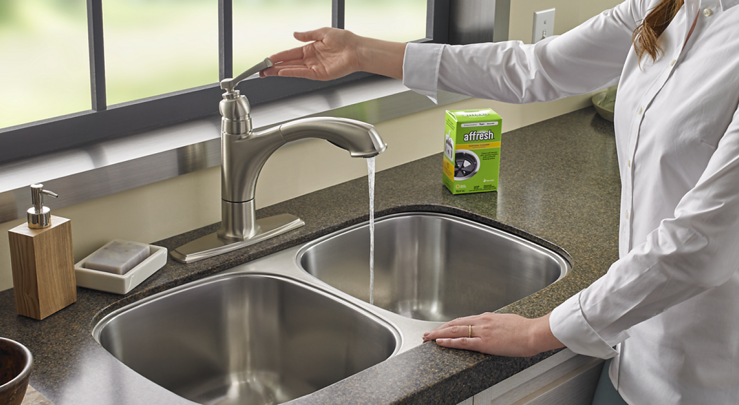 A person with an affresh® disposal cleaner tablet turning on a sink faucet 