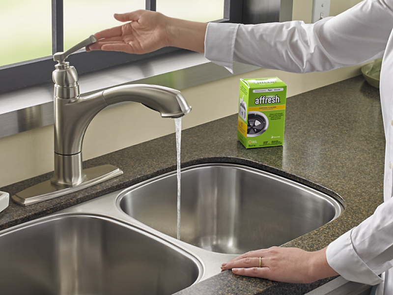 A person with an affresh® disposal cleaner tablet turning on a sink faucet 