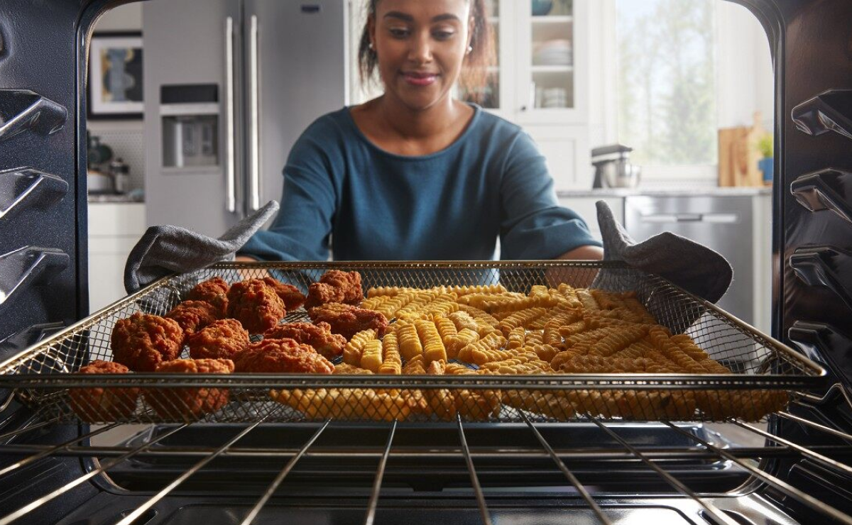 Person removing chicken strips and french fries from an oven