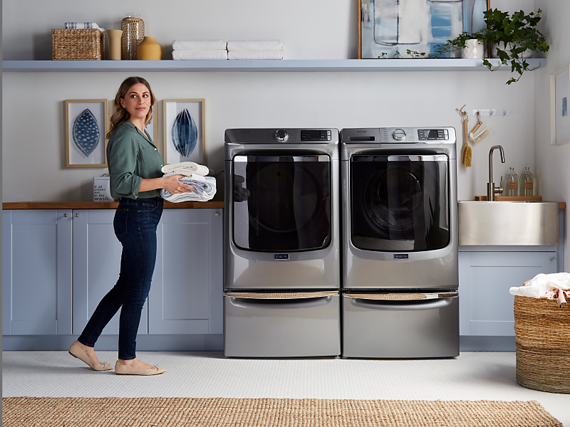 Person holding folded towels next to Maytag® front load washer and dryer