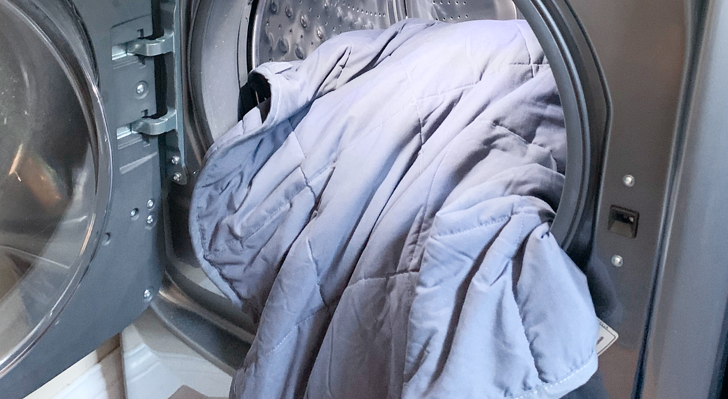 Pale blue comforter halfway inside of front load washing machine with door open