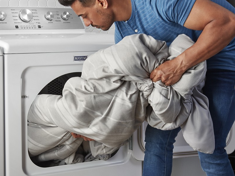Person loading large white comforter into dryer 