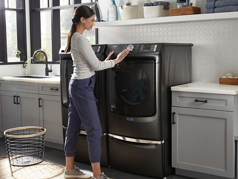 A woman programming a Maytag® dryer setting in a modern laundry room.