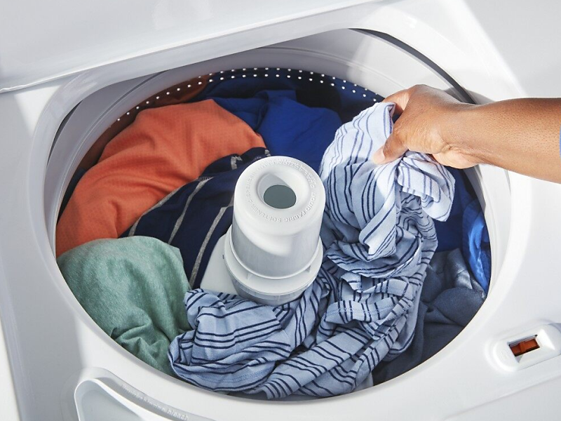 A woman adding laundry to a Maytag® top load washing machine.