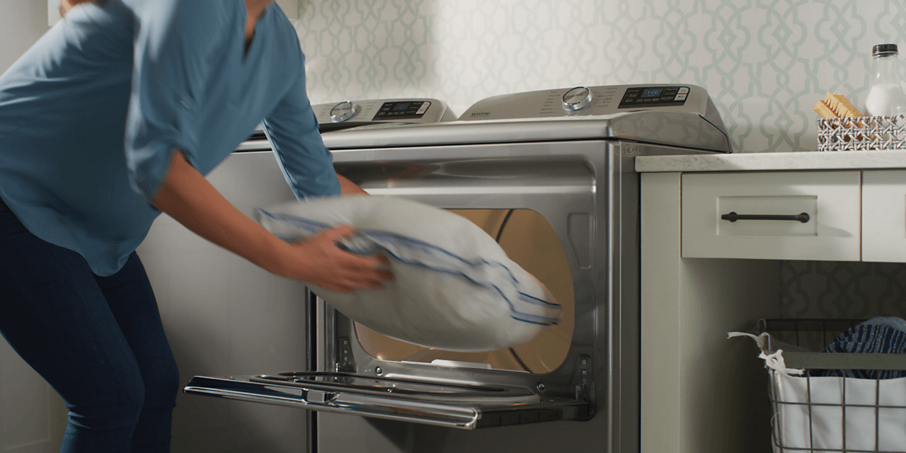 Woman loading a pillow into a Maytag® dryer