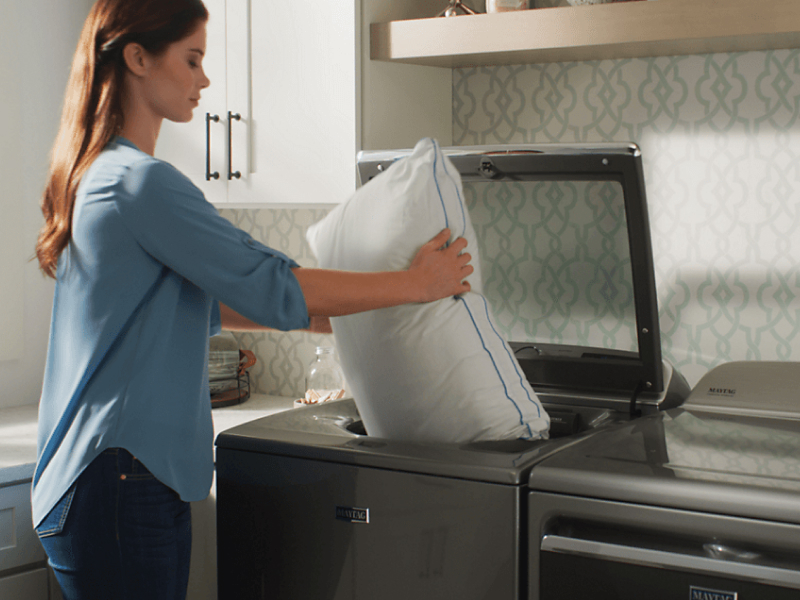 Woman loading a pillow into a Maytag® top loading washer