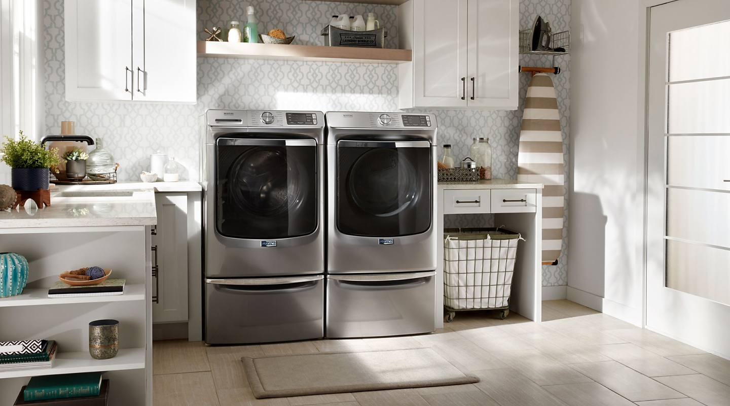 Silver Maytag® front load washer and dryer pair on pedestals in laundry room