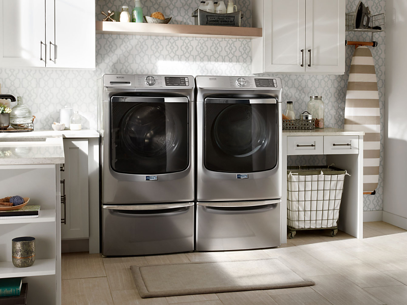 Silver Maytag® front load washer and dryer pair on pedestals in laundry room