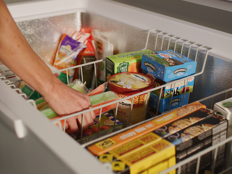 Person placing popsicles in the storage basket of a chest freezer