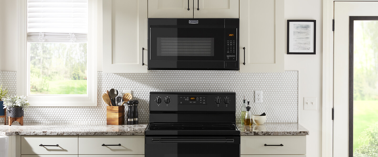 Black over-the-range microwave in white cabinets.