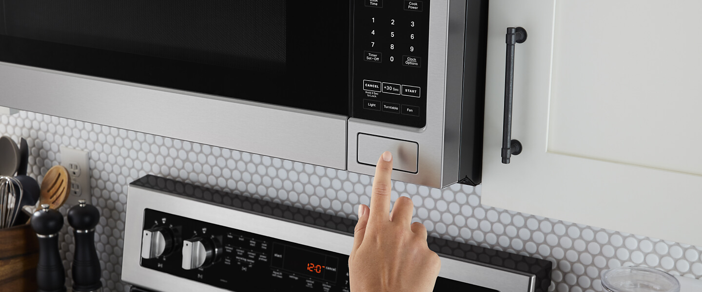 Hand pressing push button on over-the-range microwave.