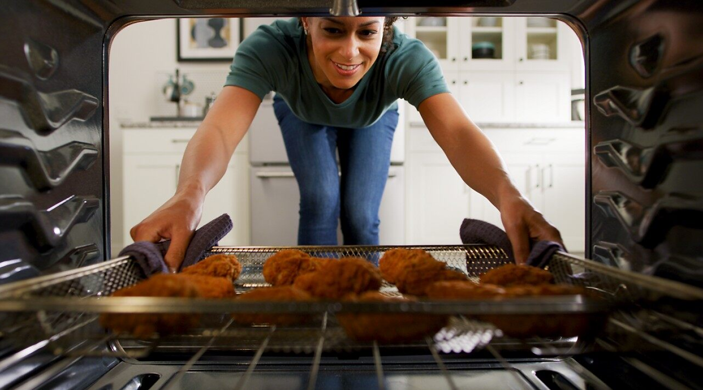 A woman placing a tray of chicken tenders into an oven to air fry.