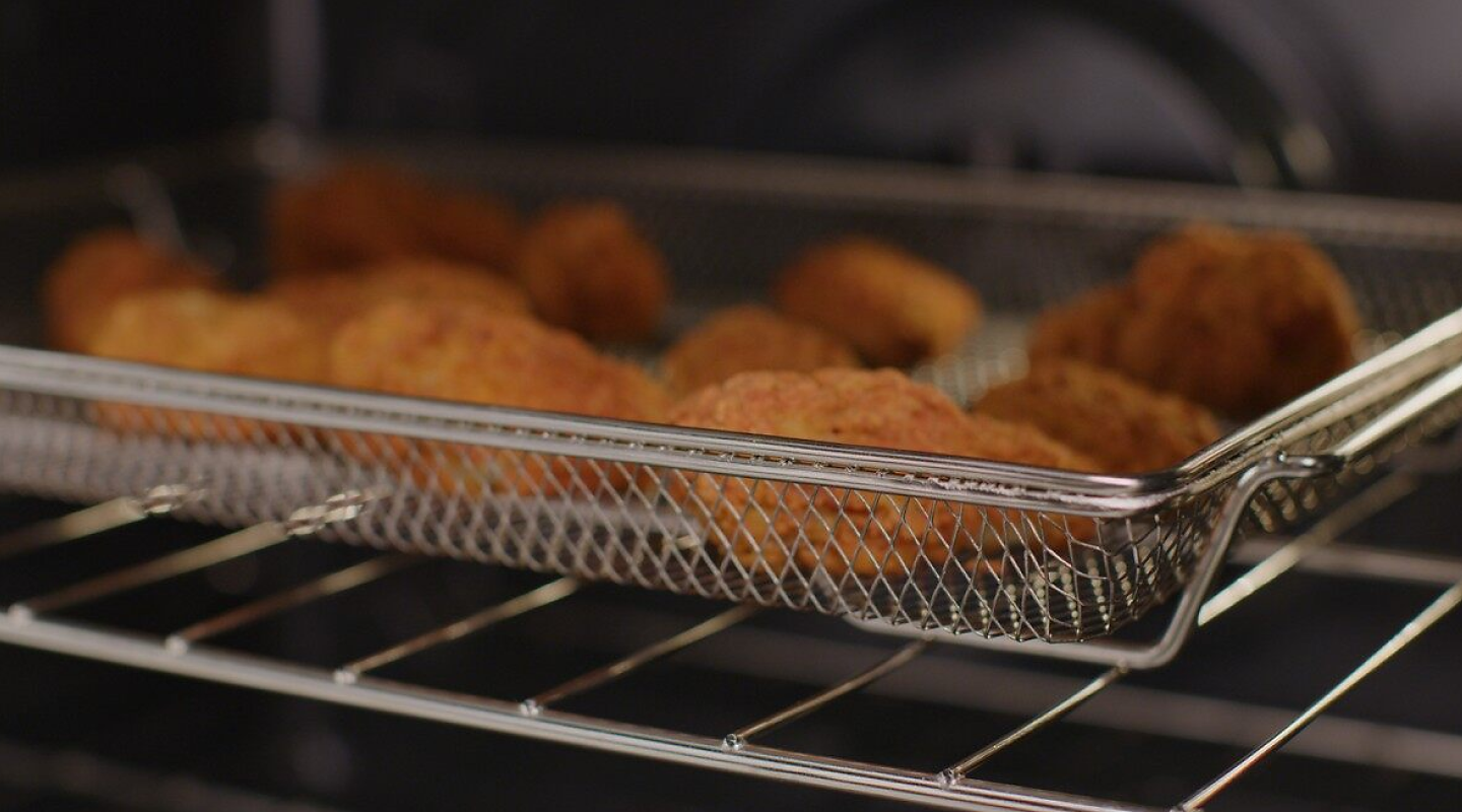 A basket of chicken tenders air frying in an oven.