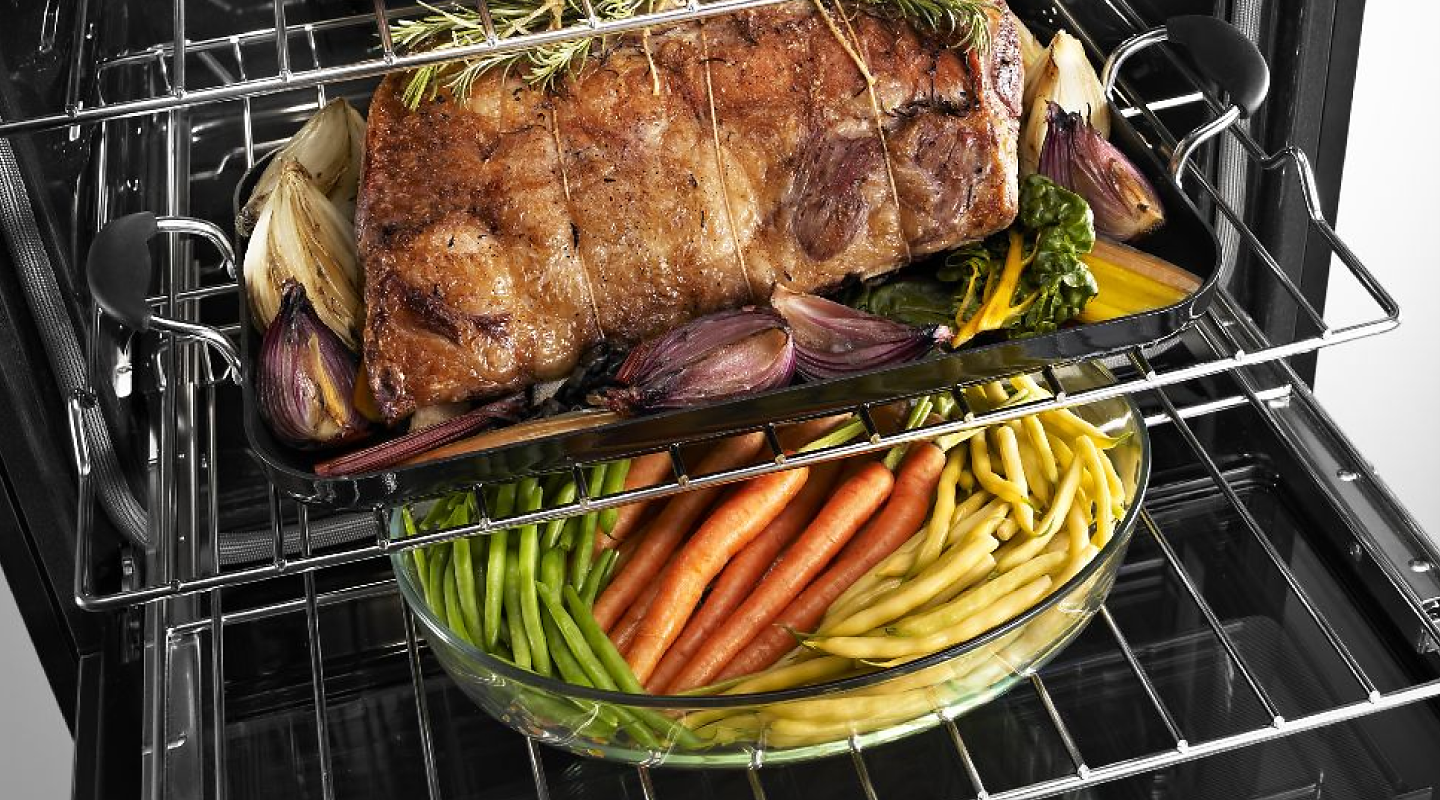 Roasted meat placed on the rack above a baking pan filled with vegetables.