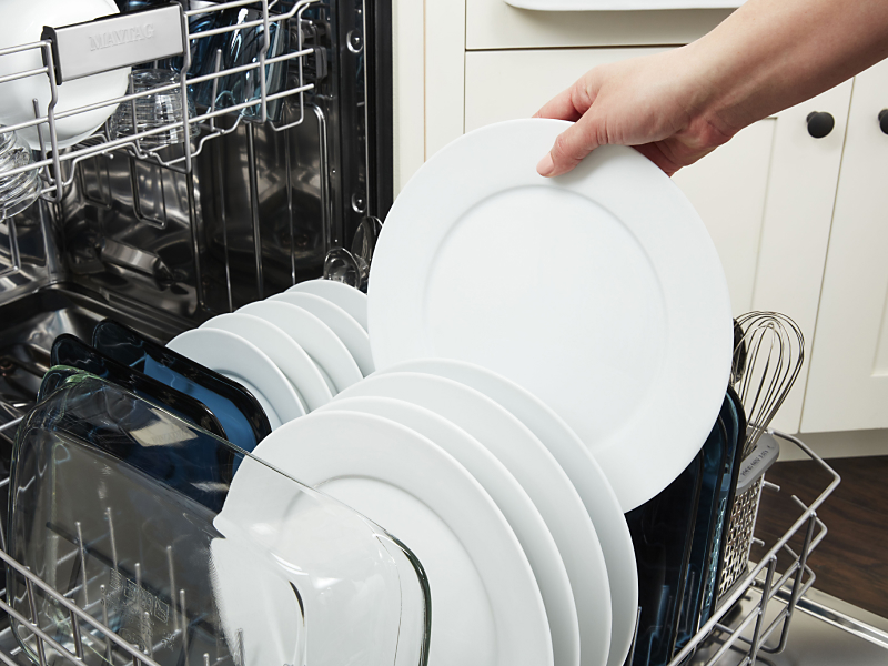 A person unloading a clean dish from a dishwasher rack 