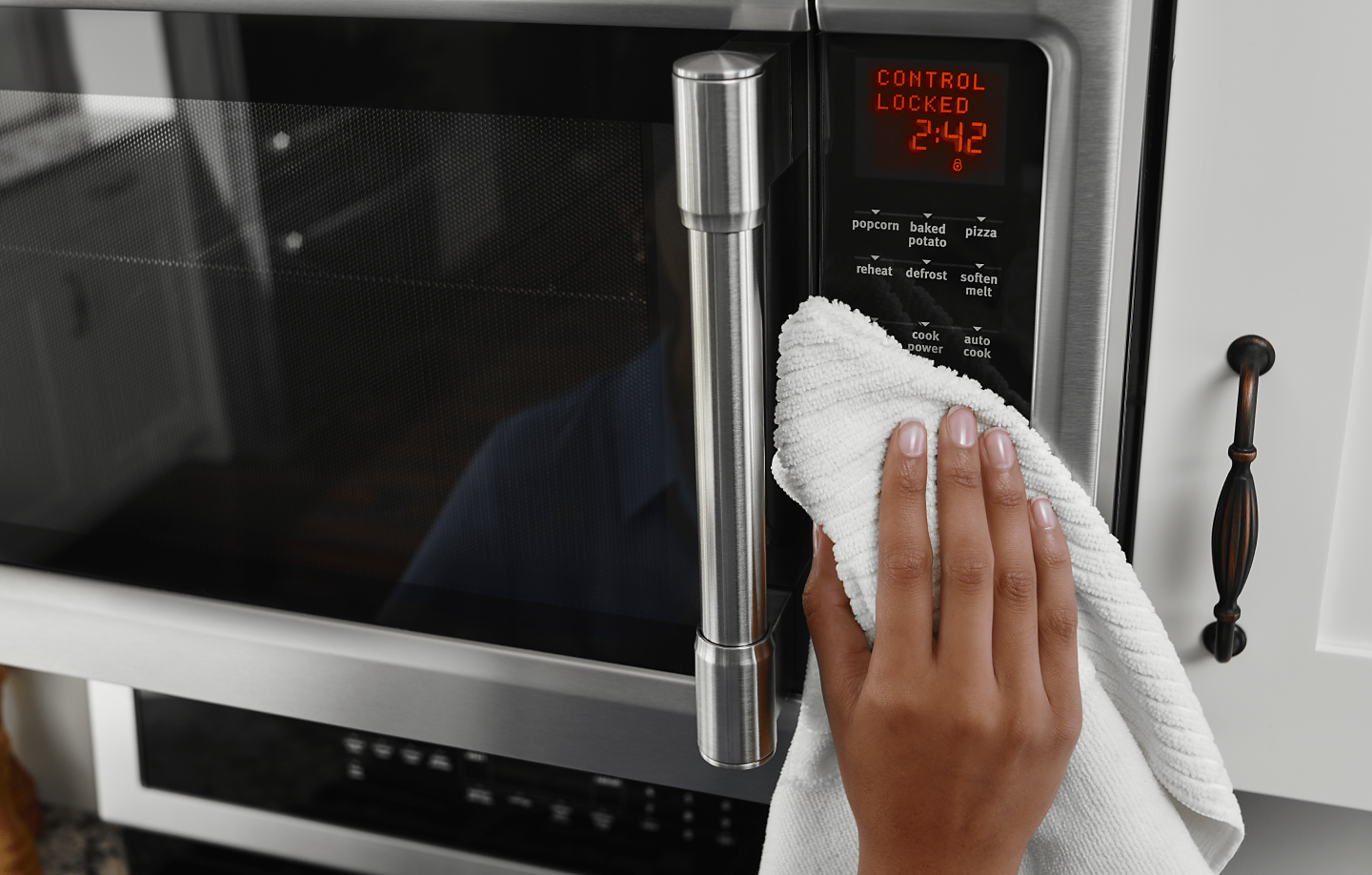 Hand holding white towel wiping microwave control panel