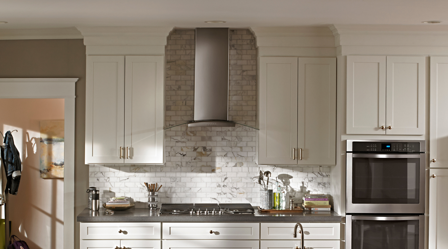 Wall mount canopy range hood in front of tile backsplash in white cabinetry.